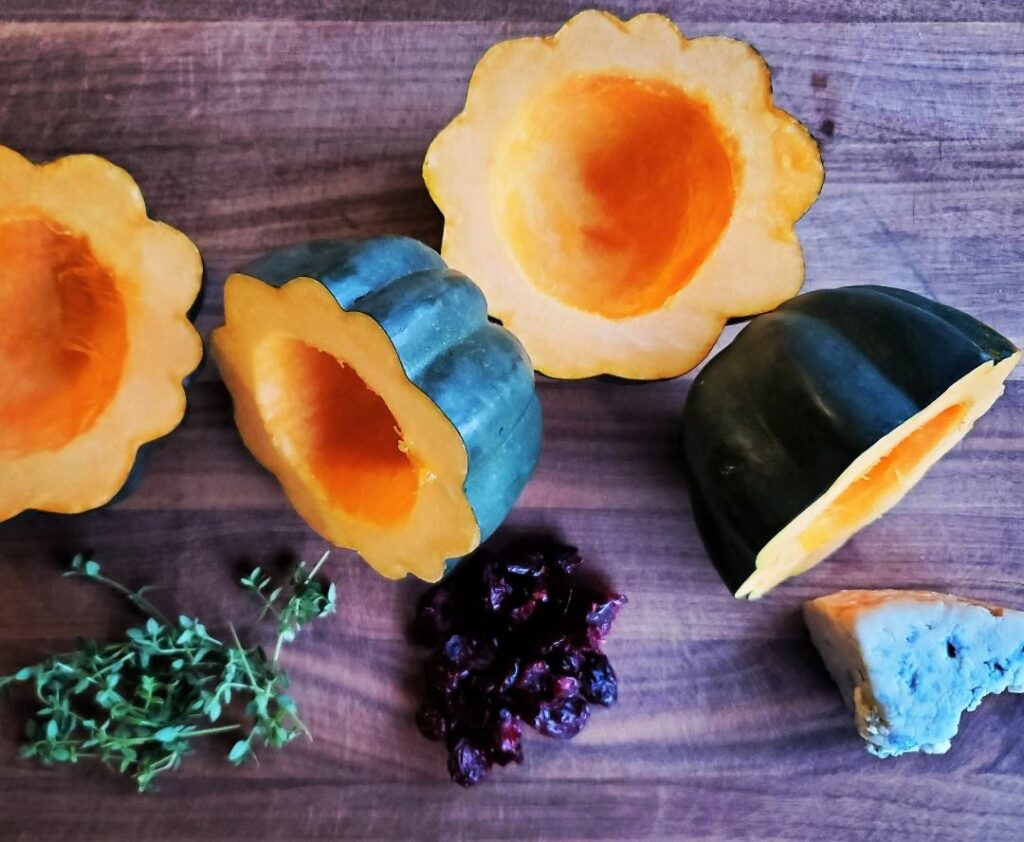 Cut acorn squash on cutting board with thyme, dried cranberries, and smoked blue cheese.