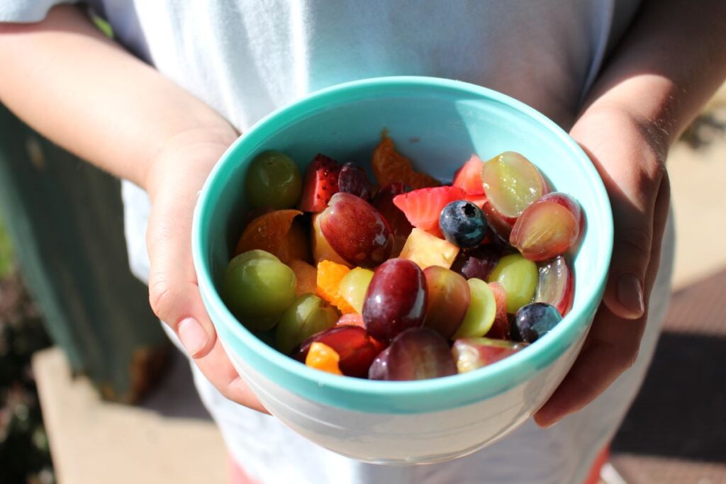 Green & purple grapes, blueberries, strawberries, oranges, and pineapples mixed together in a bowl being held by the birthday girl.
