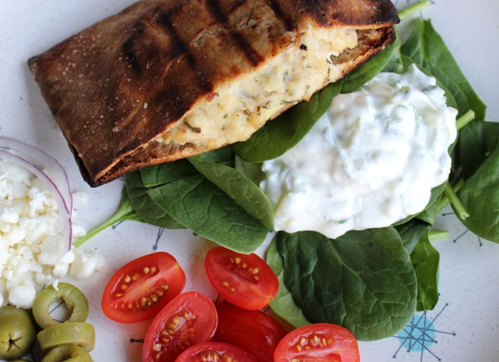 Whole wheat pita stuffed with Greek seasoned ground chicken and grilled to perfection. Plated with a side of tzatziki, fresh spinach, halved cherry tomatoes, slice green olives, crumbled feta, and thinly sliced red onion.