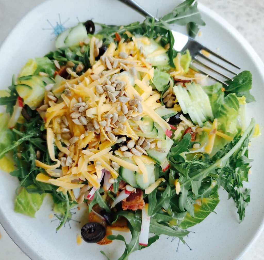 Smoked veggies are freshened up by adding them into a salad with arugula, cucumbers, black olives, crumbled bacon, radishes, honey mustard dressing and topped with crunchy sunflower seeds