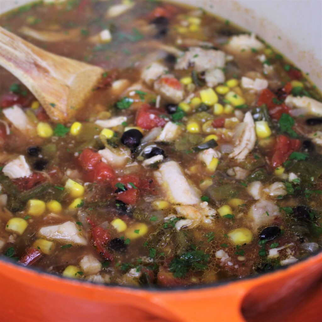 Salsa Verde Chicken Soup simmering on the stove top in an orange Le Cruset