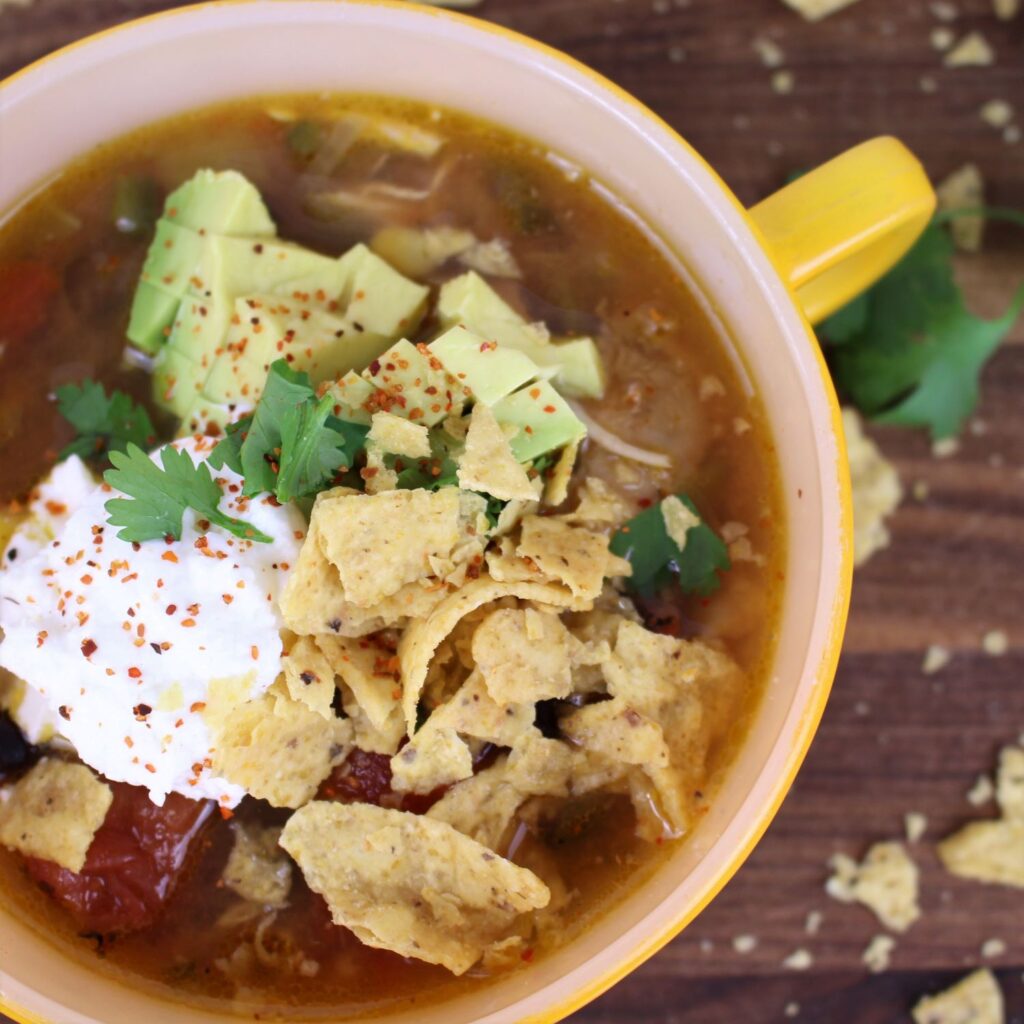 Easy Salsa Verde Chicken Soup topped with avocado, crushed tortilla chips, cilantro, and a sprinkle of tajin.