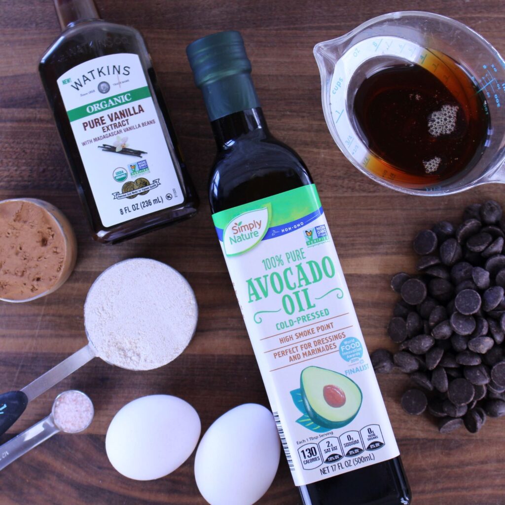 All the ingredients to make healthy fudge brownie bites which include healthy oil like avocado oil, cocoa powder, eggs, chocolate, vanilla, maple syrup, and whole wheat flour.