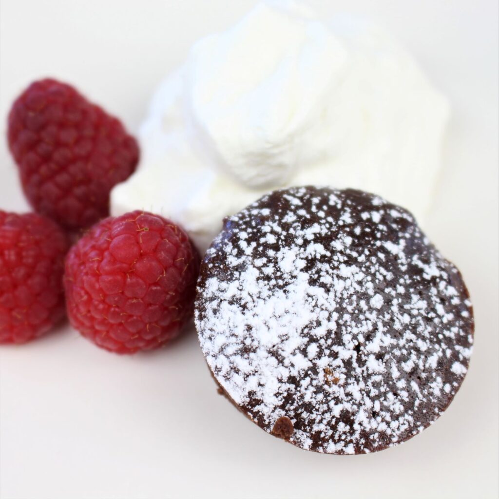 Healthy fudgy brownie bites topped with powdered sugar along side with fresh whipped cream and raspberries.