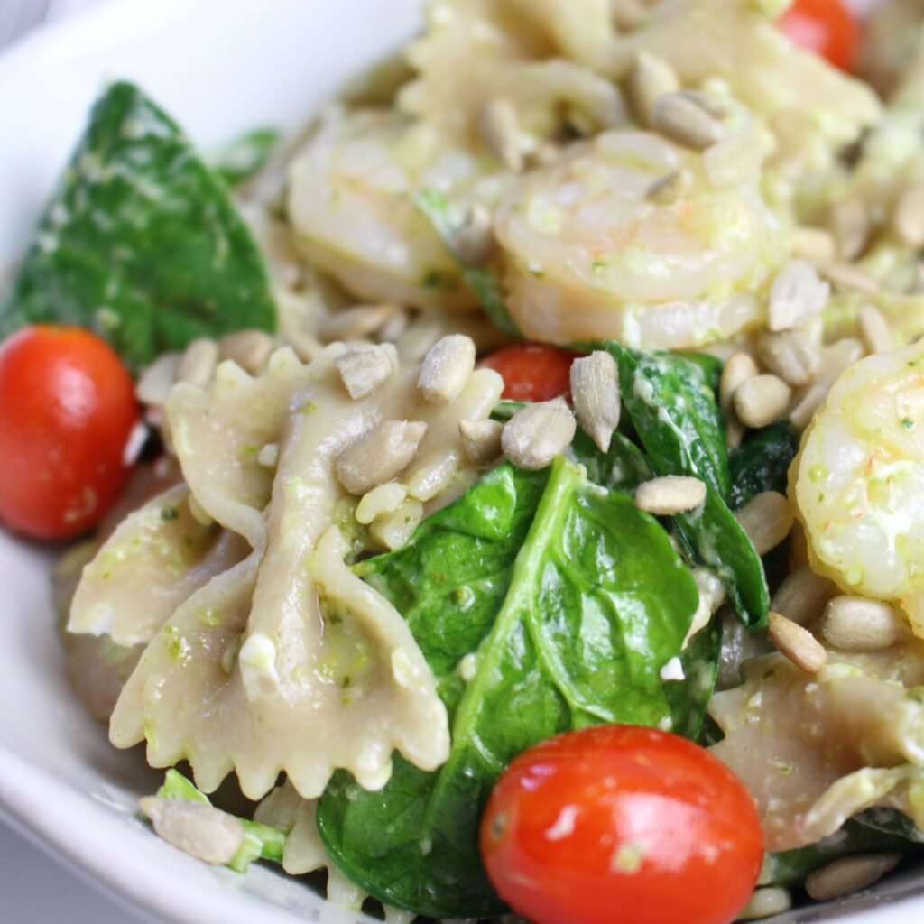 Pesto covers bowtie pasta, wilted spinach, goat cheese crumble, and cherry tomatoes in this creamy and healthy pasta dish. It's topped with sunflower seeds.