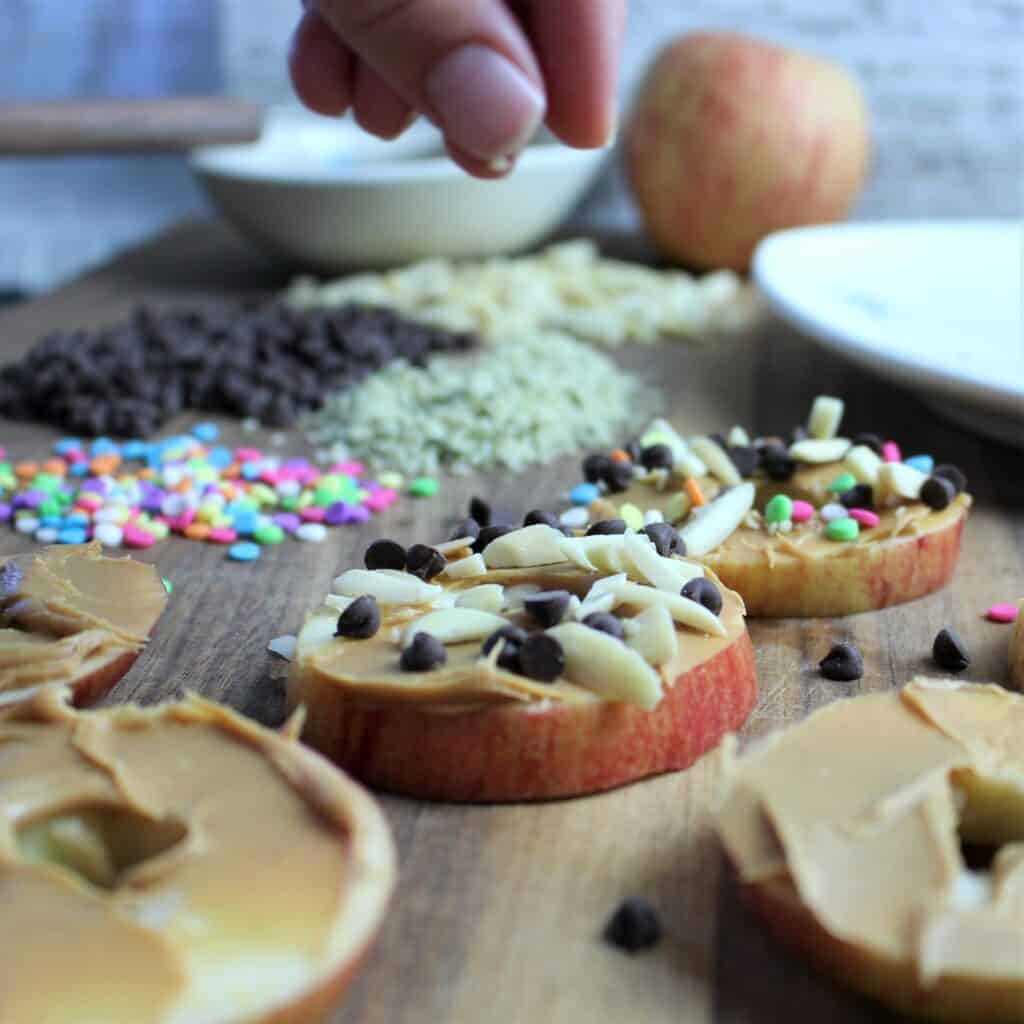 little fingers make their own apple ring donuts which are apple rings, with peanut butter and toppings