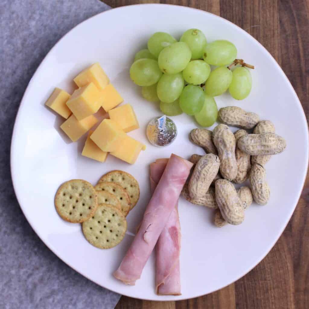 charcuterie plate with ham, crackers, cheese cubes, grapes, peanuts, and a hershey kiss