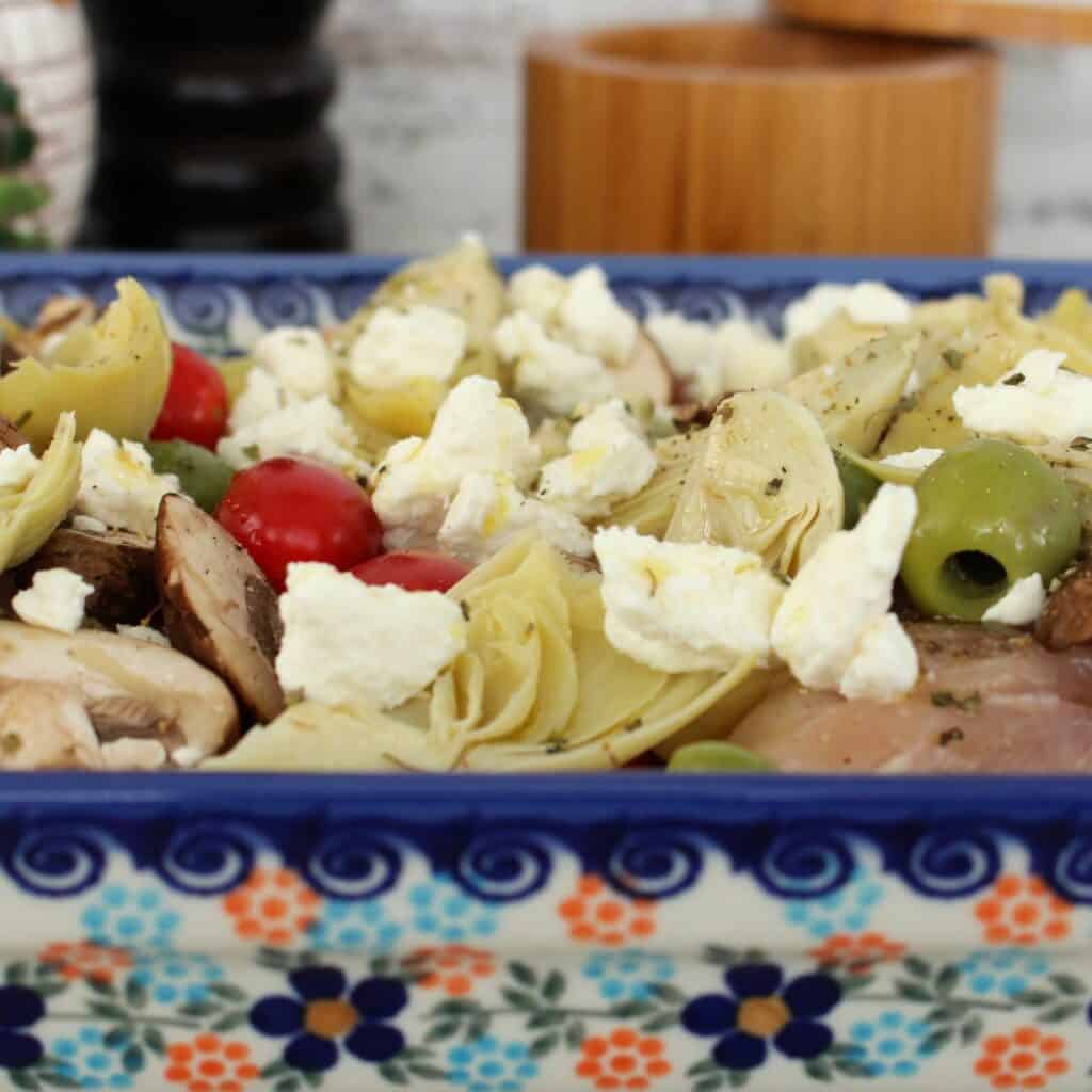 Side angle of the chicken artichoke recipe loaded with feta, cherry tomatoes, artichoke hearts, and olives.