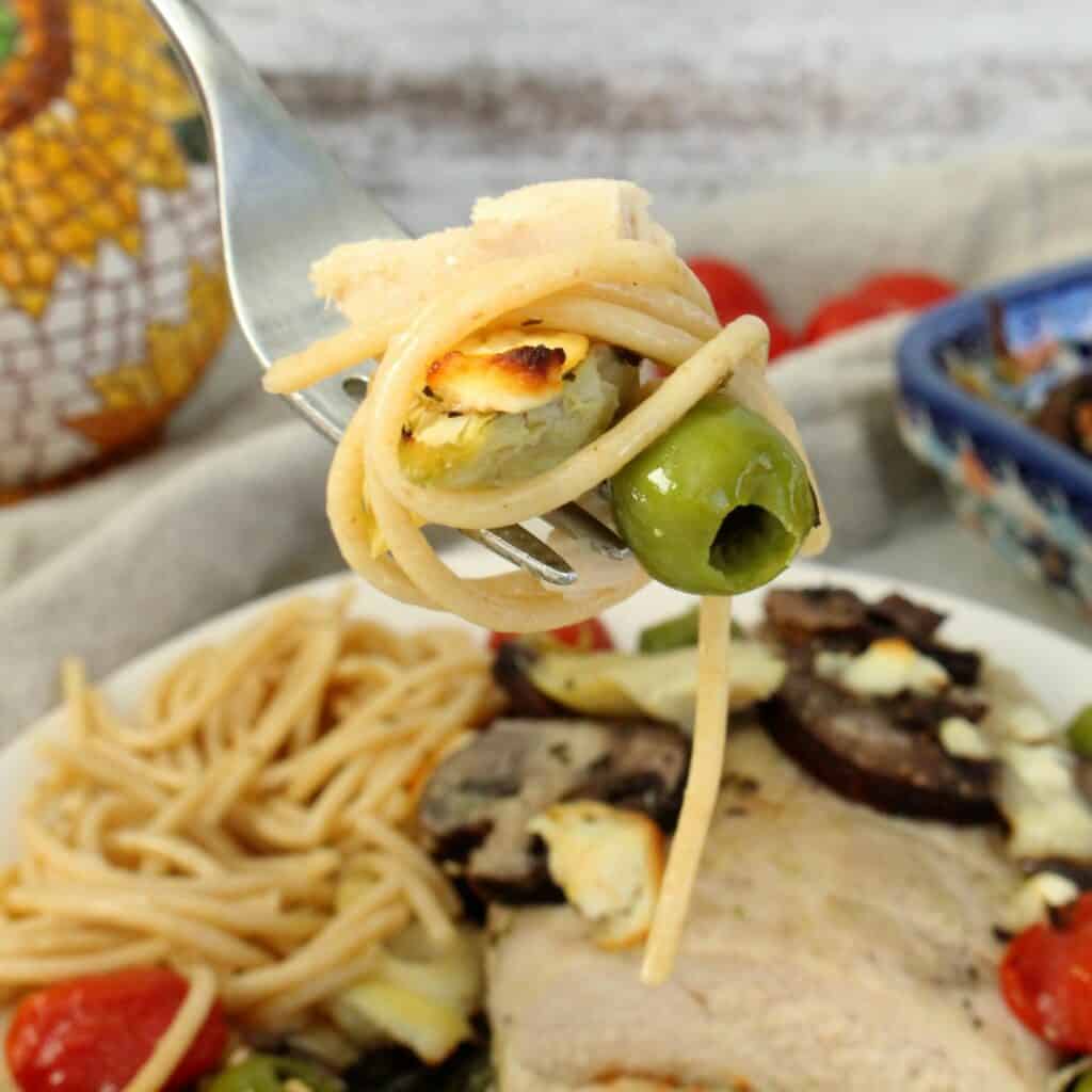 Fork full of pasta, olive, feta, chicken and artichoke.