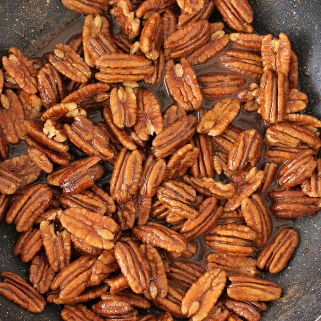 Pecan halves in pan with maple syrup and spices