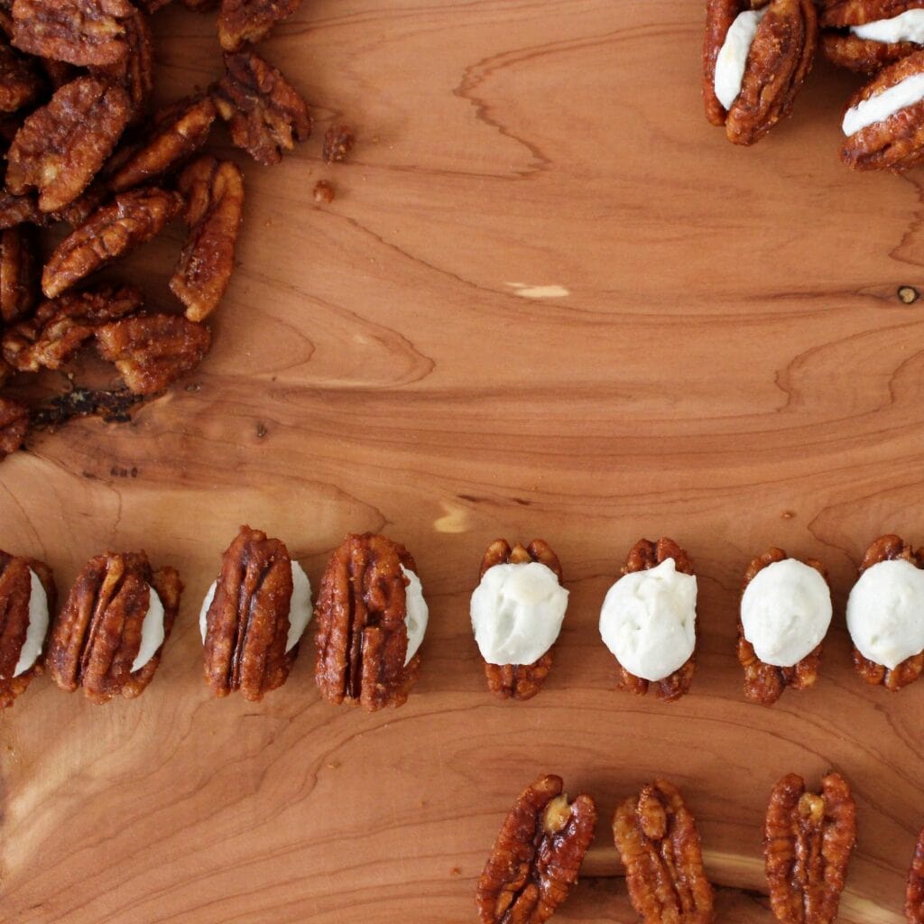 pecan halves lined up being filled with blue cheese cream and topped with another pecan half.