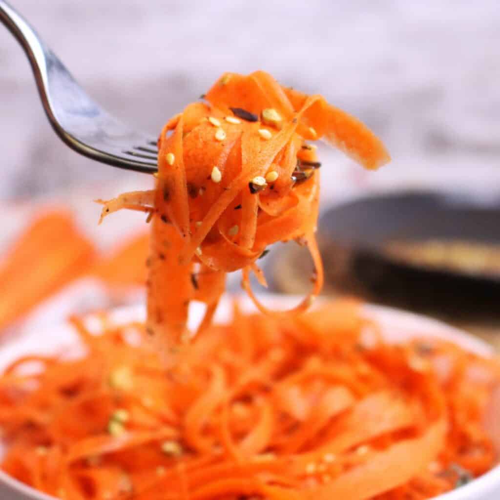 A forkful of carrot ribbons tossed in a fresh lemon juice, olive oil, maple syrup, and ginger dressing, topped with Dukkah.