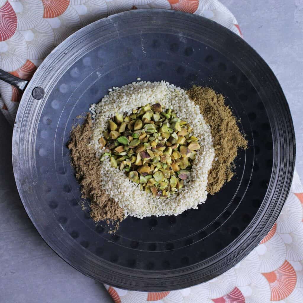 Chopped pistachios, sesame seeds, coriander, and cumin in a pan for toasting.