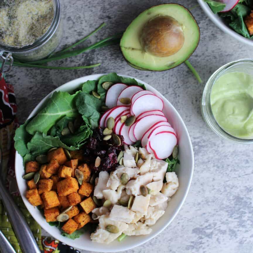 Sweet Potato Nourish Bowl with chicken, baby kale, radishes, and roasted sweet potatoes with an avocado dressing on the side.