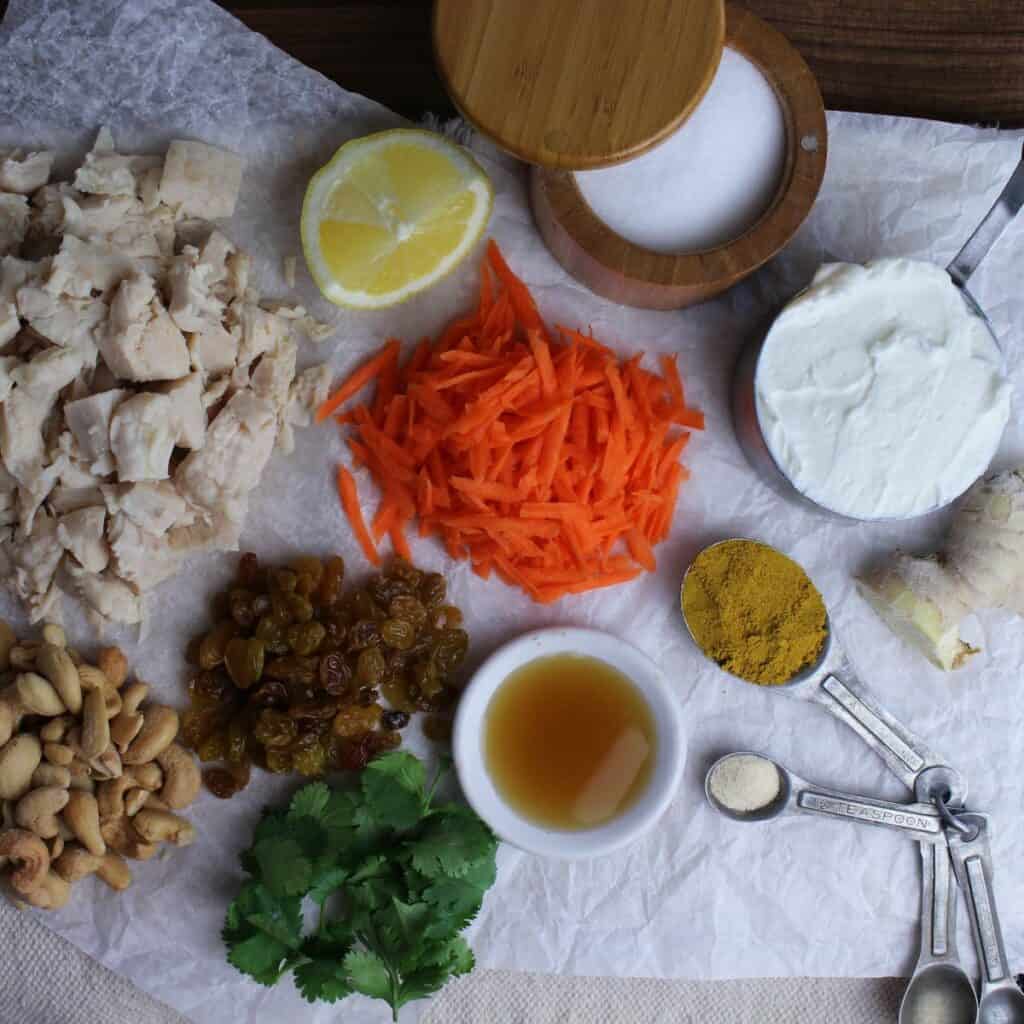 Curry chicken salad without celery recipe ingredients are chicken, carrot, golden raisins, greek yogurt, honey, cilantro, cashews, a squeeze of lemon, curry powder, garlic, ginger, and a pinch of salt.