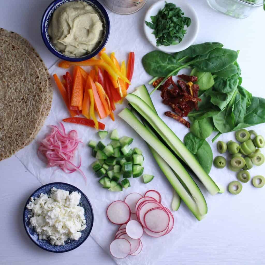 Crunchy veggies, whole grain wraps, hummus, feta, olives, and fresh parsley all ready to be rolled into a delicious wrap.