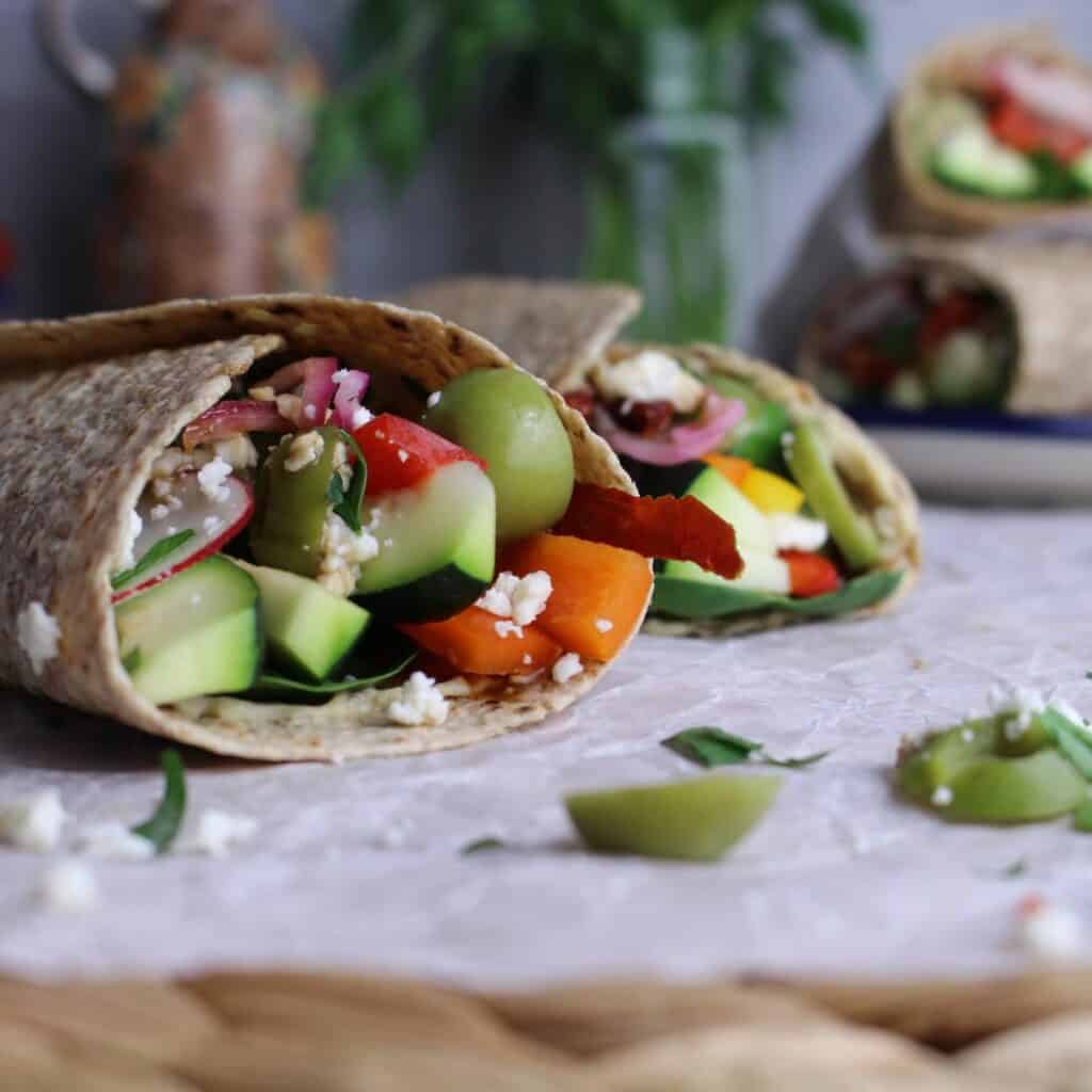 Whole grain tortillas rolled up with fresh and crunchy veggies, feta, with olives spilling out.