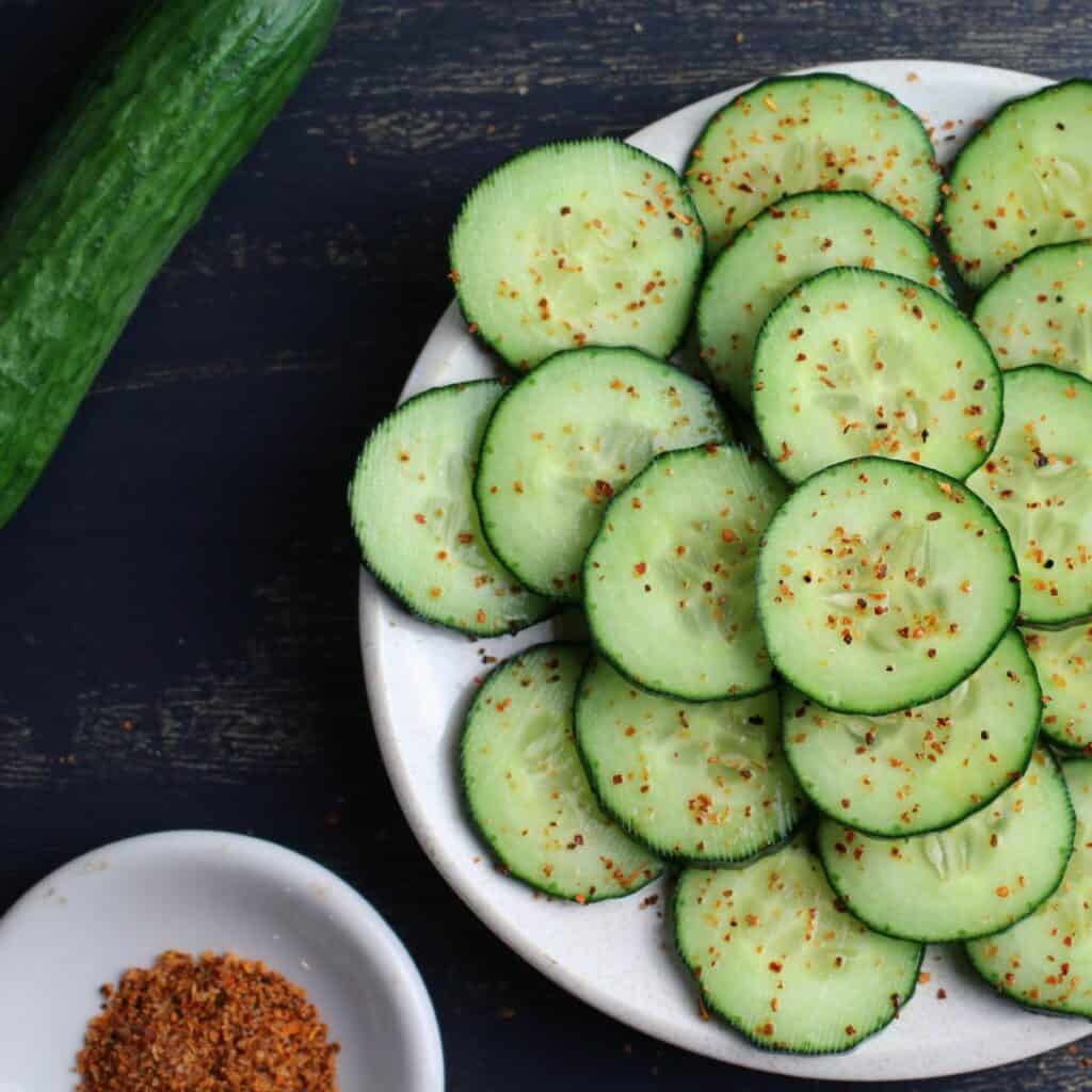Cucumber slices arranged on a platter with tajin sprinkled on top.