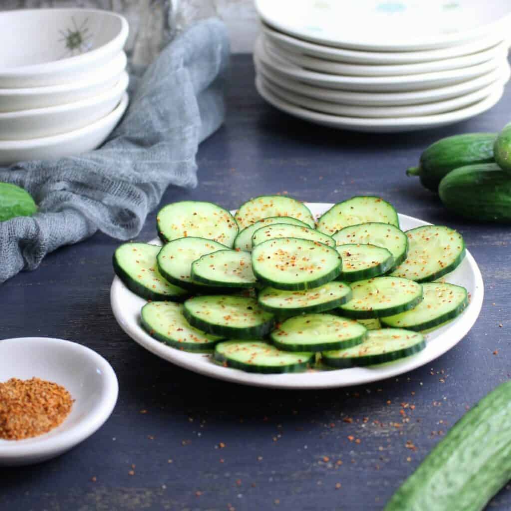Cucumber slices arranged on a plate with a sprinkling of Tajin, a tangy spice blend, on each piece.