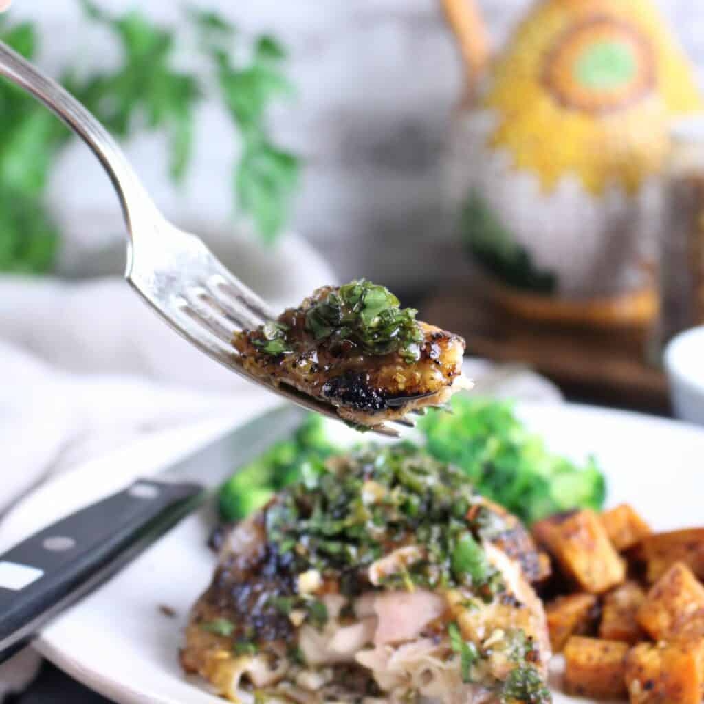 A fork full of perfectly grilled chicken thighs topped with herby chimichurri.