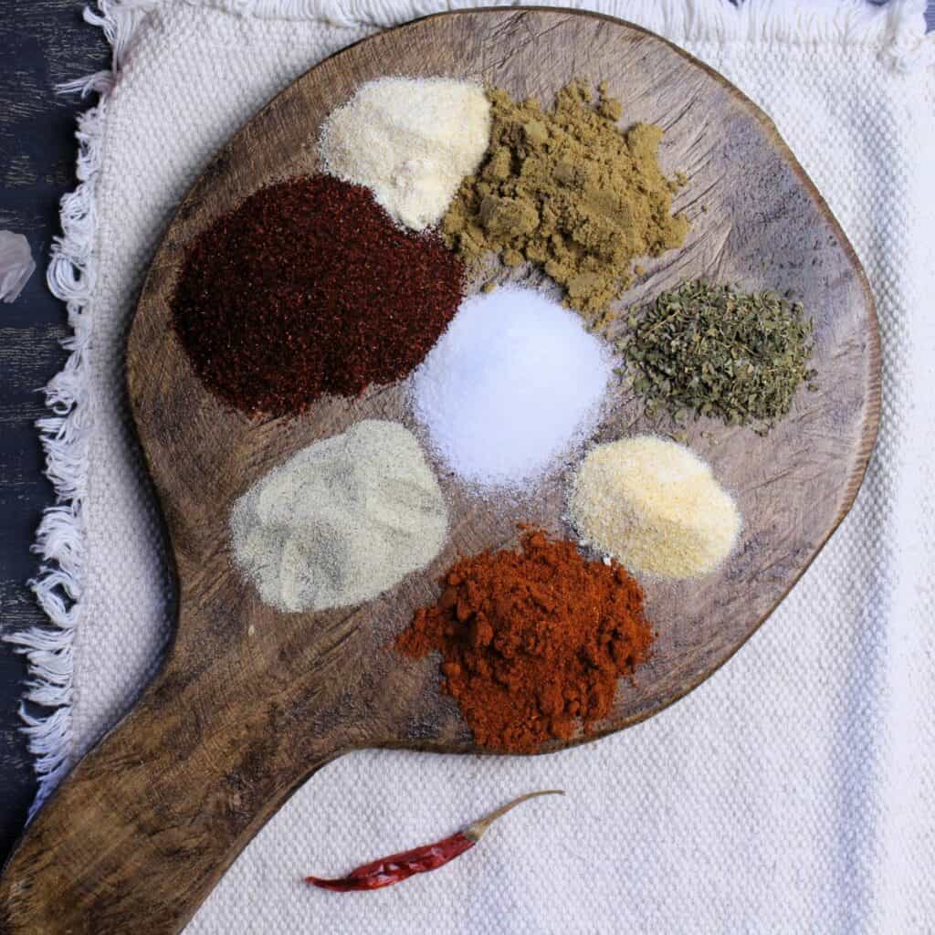 Spices for taco seasoning blend on wooden paddle.