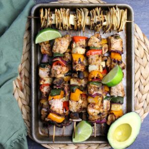 Grilled chicken fajita kabobs on serving tray with limes and avocado.
