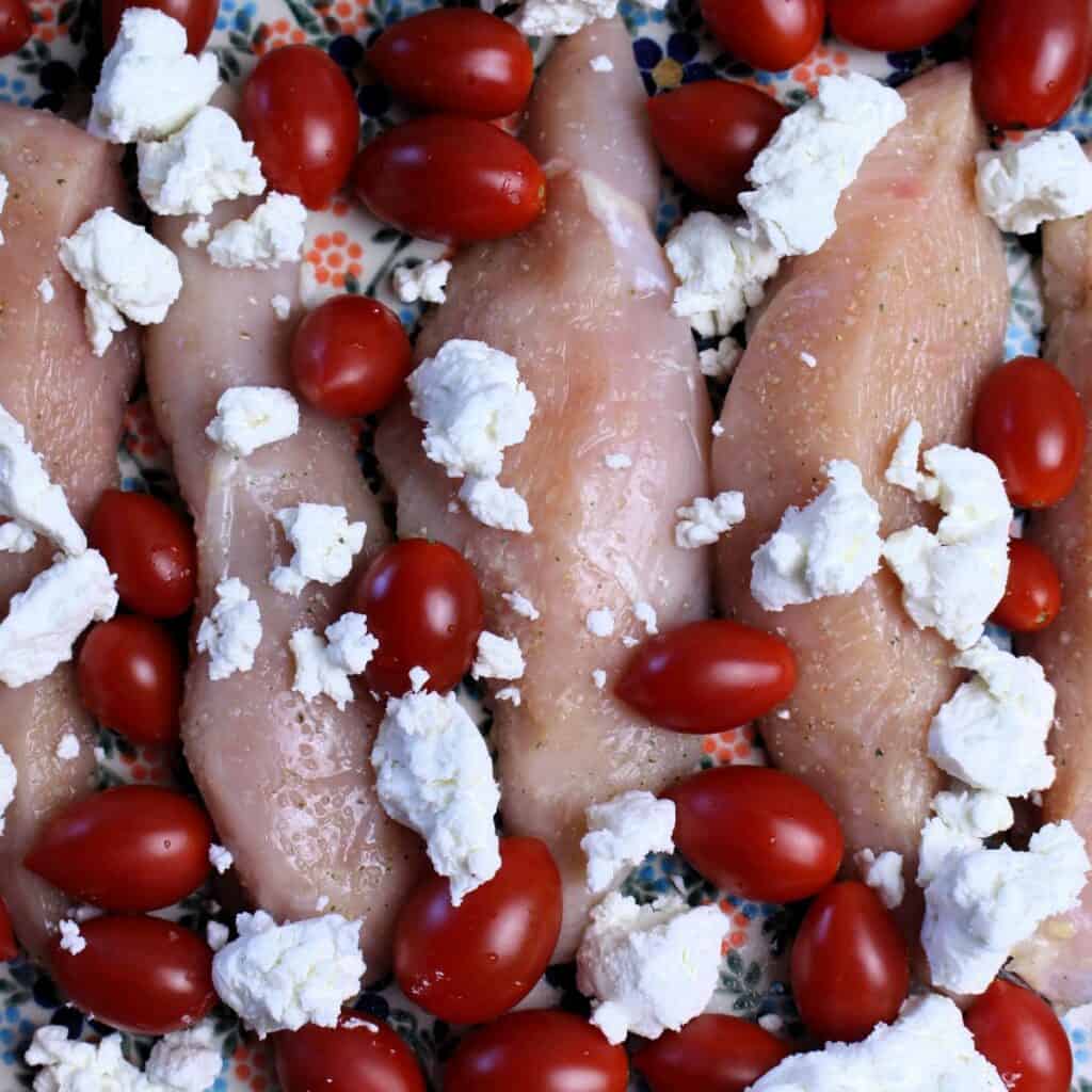 Chicken tenders, cherry tomatoes, and goat cheese crumbles in a dish and ready to go in the oven. 
