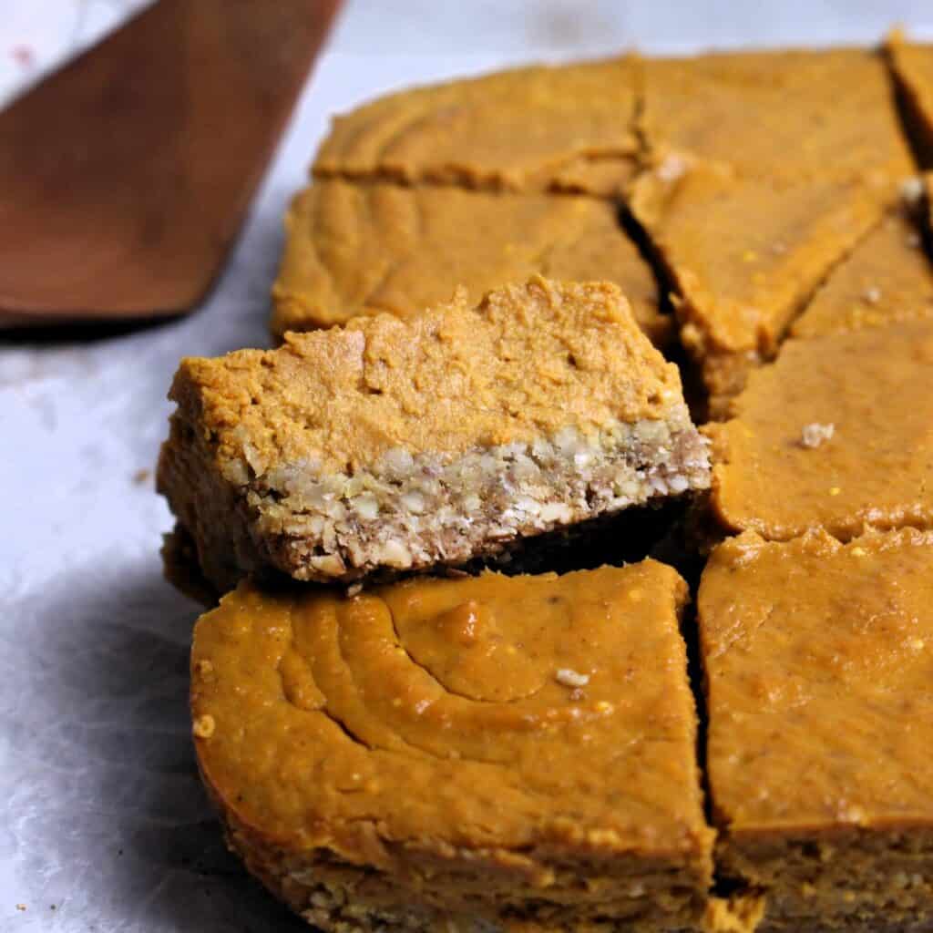 A pumpkin pie bar raised up revealing the oat crust and thick creamy pumpkin filling.