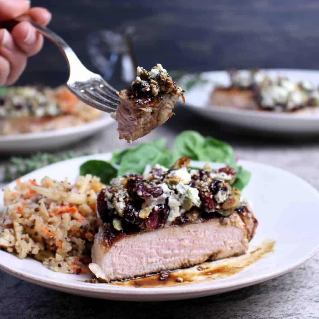 Forkful of pork chop with dried cranberries and goat cheese with balsamic reduction.