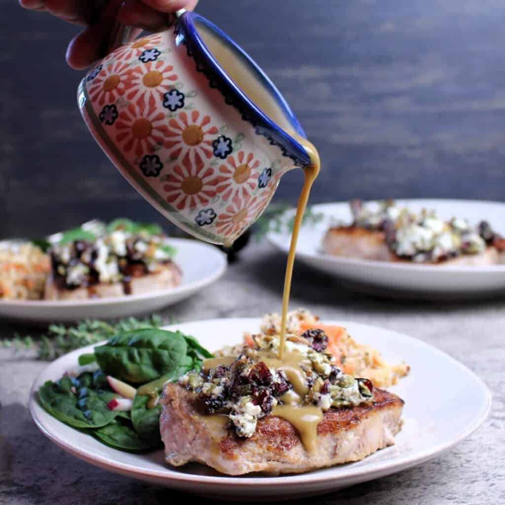 Dijon pan sauce drizzled on top of seared pork loin chops with goat cheese cranberry crumble.