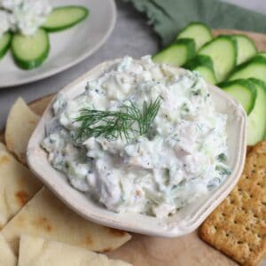 Chicken salad with tzatziki served on a platter with cucumbers, crackers, and pita.