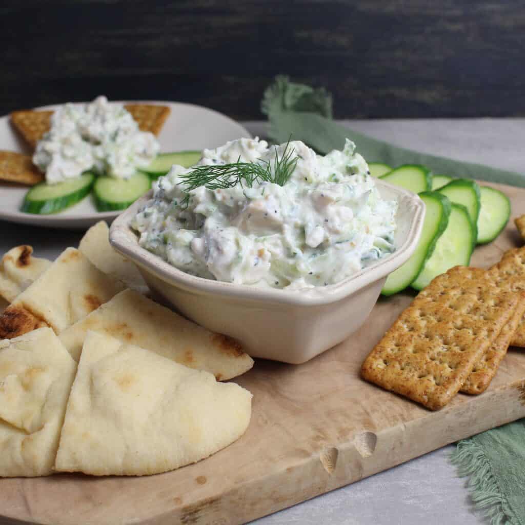 Chicken Salad with Tzatziki served on a wooden platter with cucumber slices, crackers, and naan.