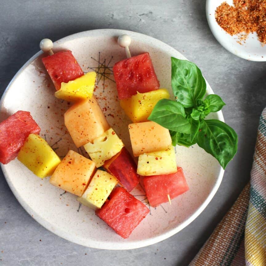 Fruit skewers with Tajin plated with a sprig of basil.