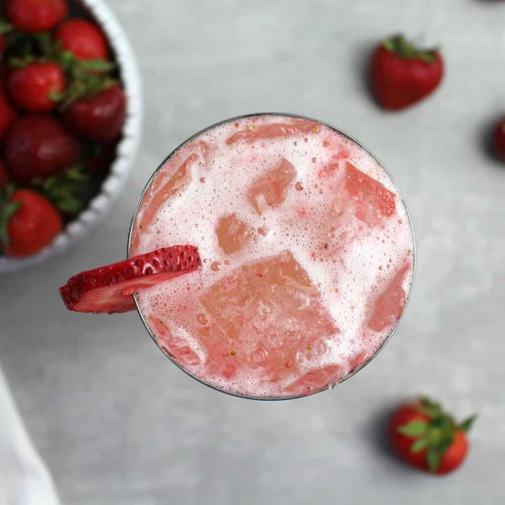 Overlooking a light pink Strawberry Spritz cocktail with a strawberry slice on the side of the wine glass.