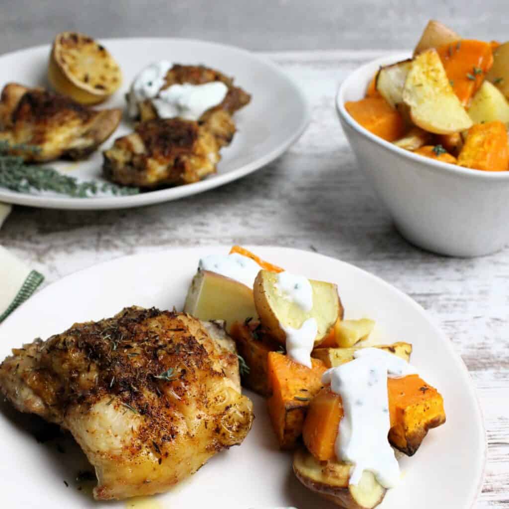 Plated tray baked chicken thighs and root vegetables with a creamy chive sauce.