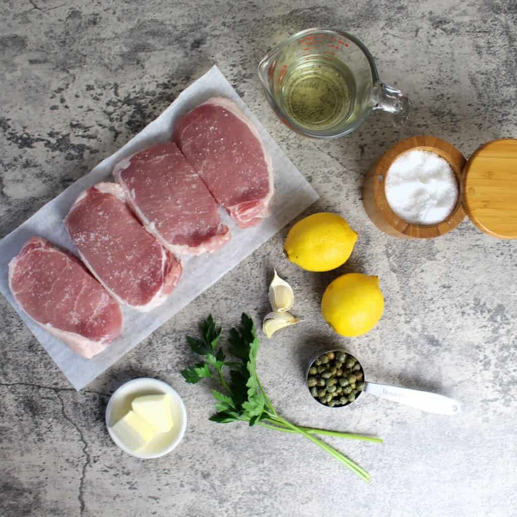 Ingredients needed to make pork piccata: lemons, capers, pork loin chops, parsley, butter, white wine, garlic and salt.