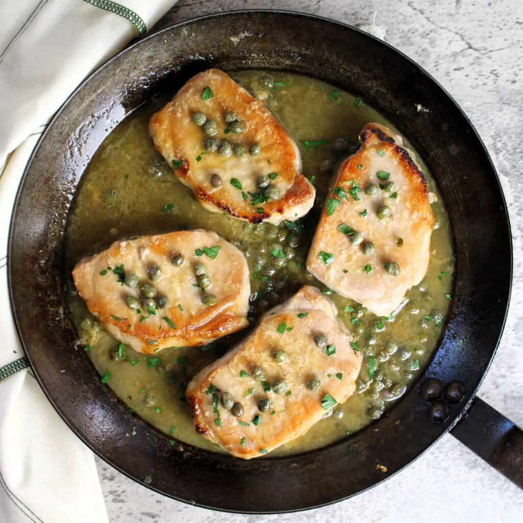 Pork chops with lemon caper sauce in pan.