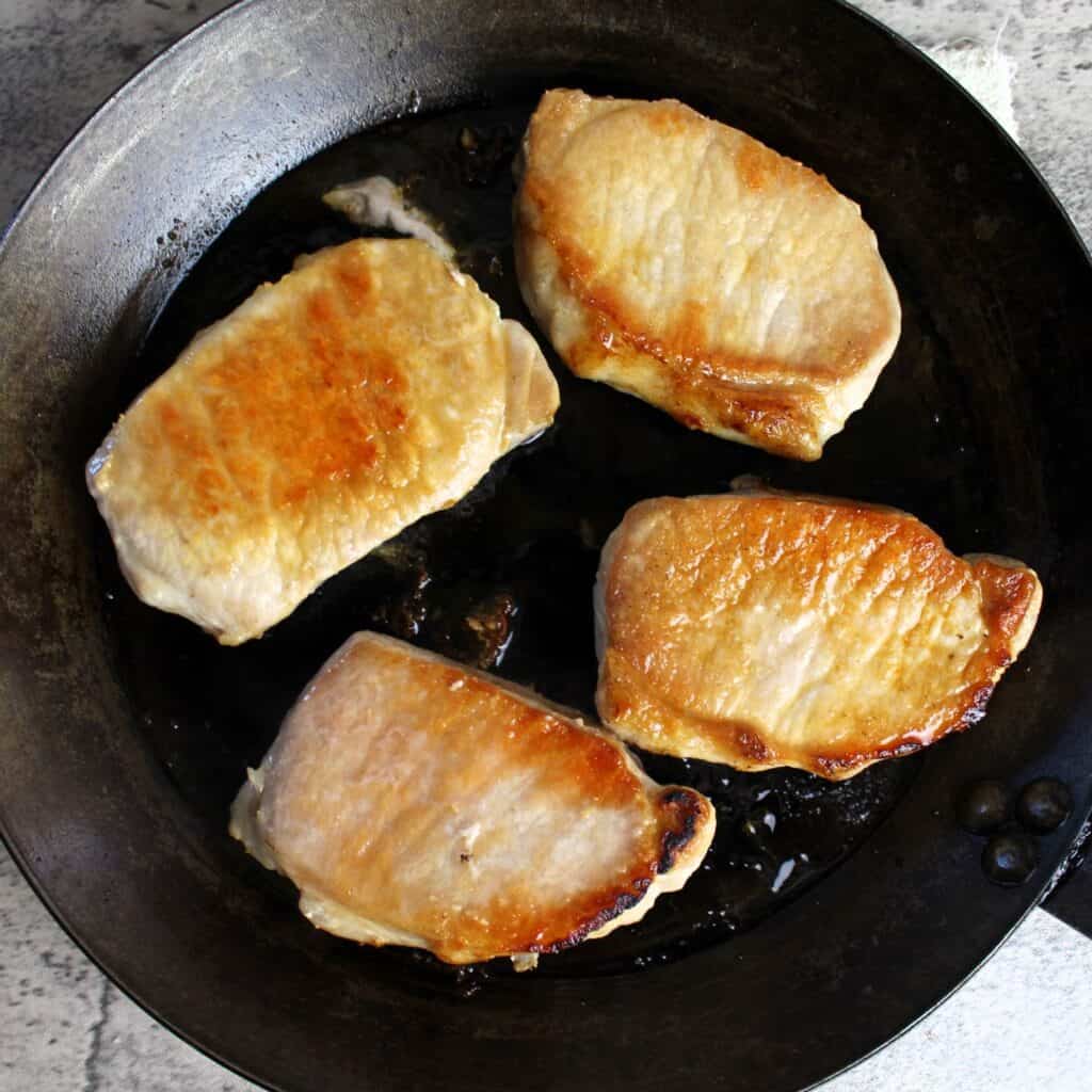 Pork chops cooking in cast iron pan.