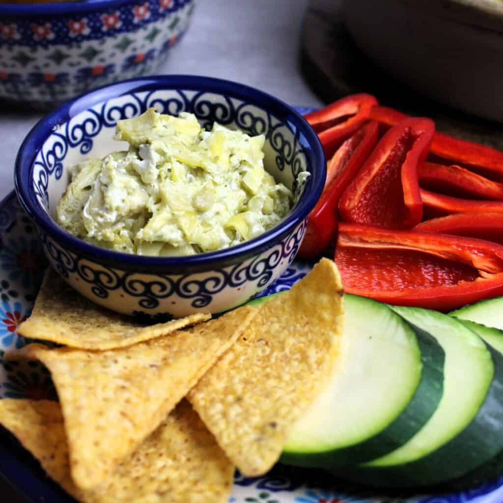 Artichoke pesto dip plated with veggies and chips for dipping.