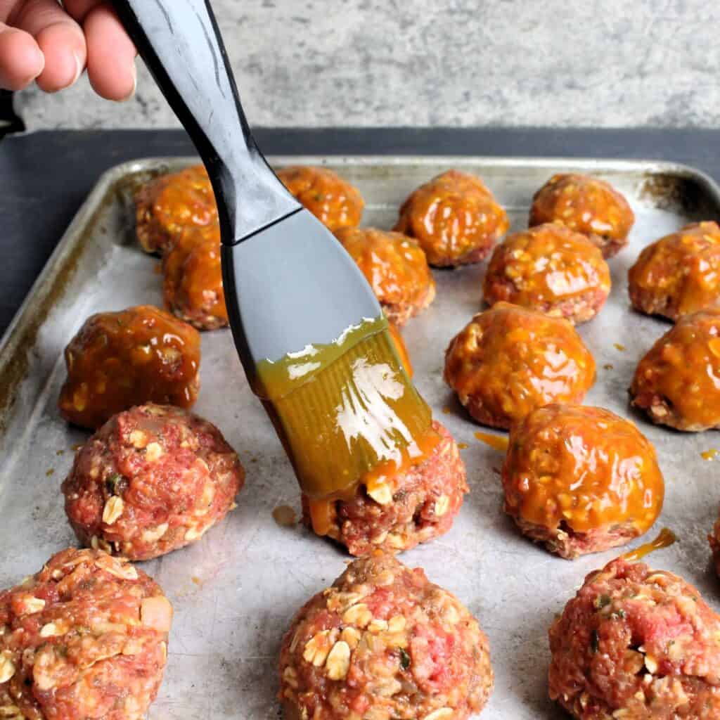 Meatballs getting glaze brushed on before baking.