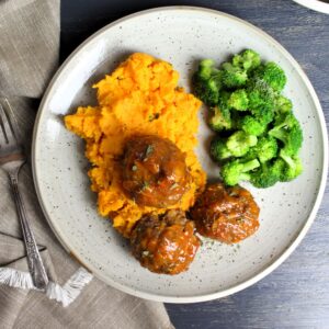 Meatloaf meatballs on top of sweet potato mash with a side of steamed broccoli plated.