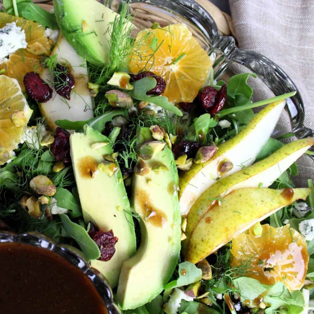 Close up of pear arugula salad with avocado, orange wheels, pear slices, and more.