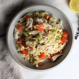 Chicken Orzo Bake in bowl with sprig of thyme and lemon wedge on side.