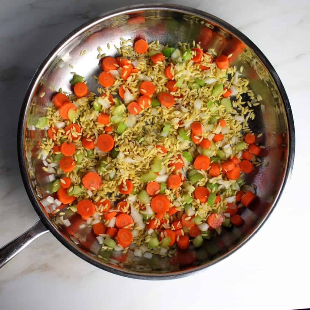 Veggies and orzo sautéing in pan.